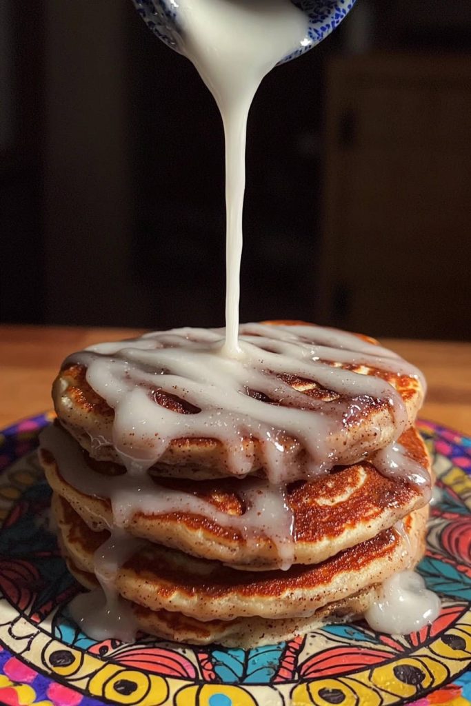 Cinnamon swirl pancakes with vanilla dream drizzle being poured from a bowl, creating a rich glaze.