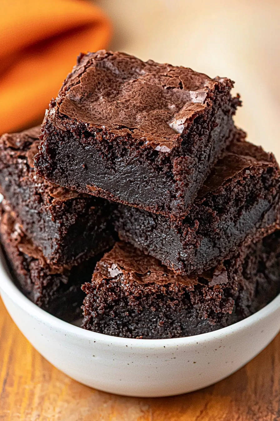 Fudgy espresso brownies stacked in a white bowl, showcasing a rich chocolate interior and crackly top.