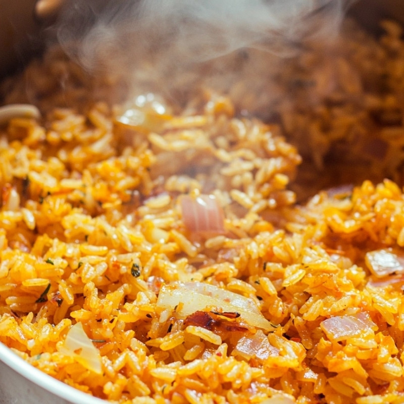 Golden rice pilaf steaming in a pot, showcasing visible onions and a rich orange hue.