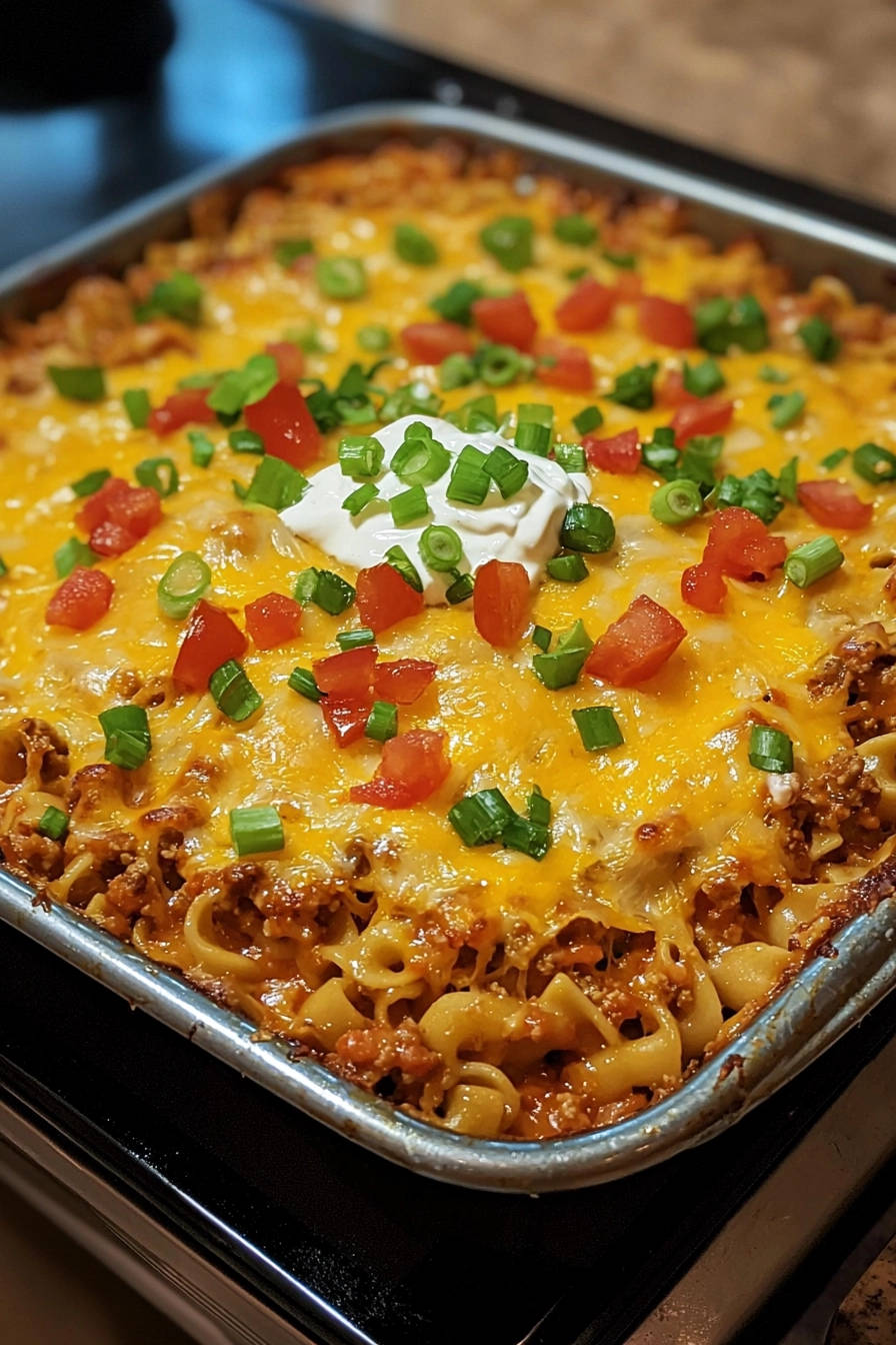 Cheesy noodle bake topped with sour cream, tomatoes, and green onions in a baking dish.