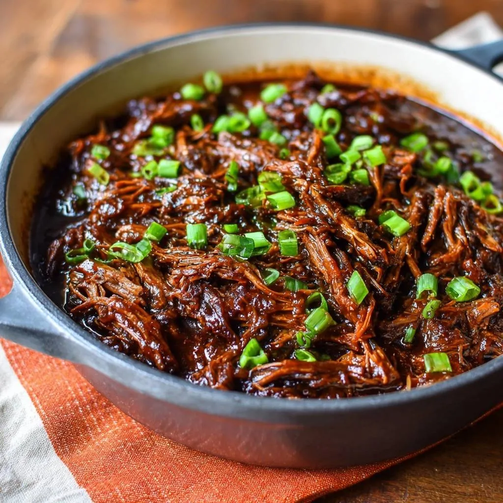 Korean-style shredded beef, tender and braised, generously garnished with fresh green onions in a cast iron pan.
