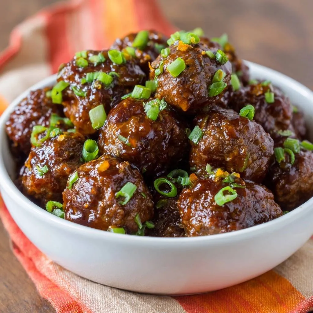 Sticky orange glazed meatballs recipe shown in a white bowl, generously garnished with chopped green onions and orange zest.