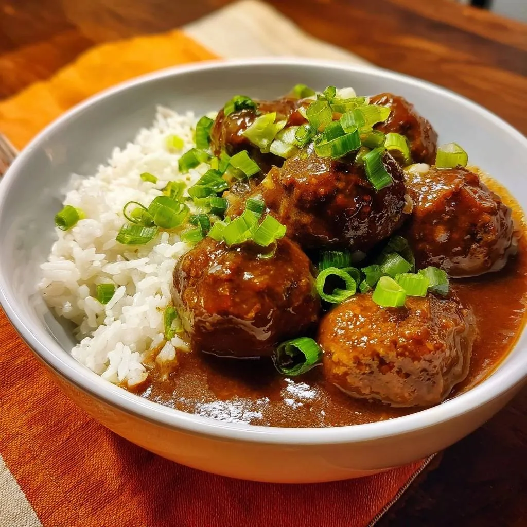 Teriyaki meatballs over rice garnished with chopped green onions, showcasing the sauce and texture.