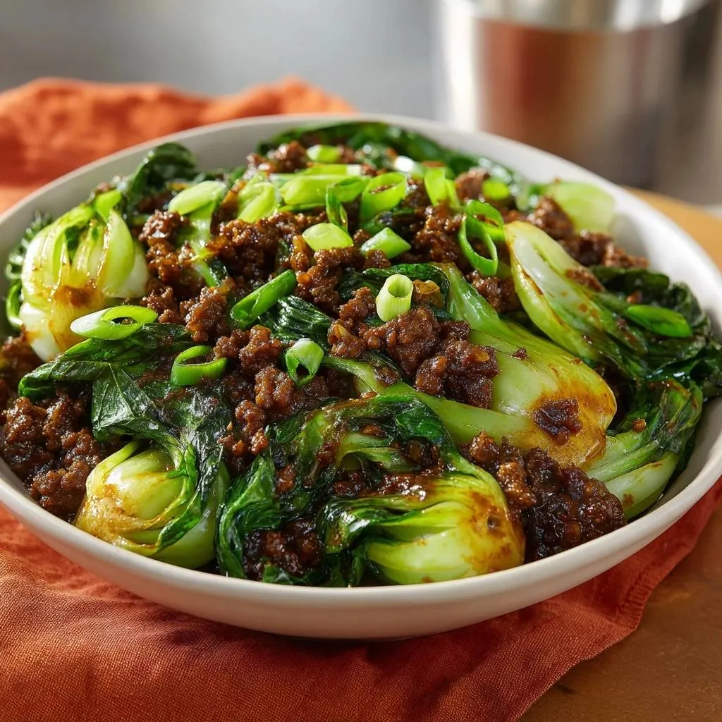 Savory beef and bok choy stir-fry in a white bowl, garnished with chopped green onions.