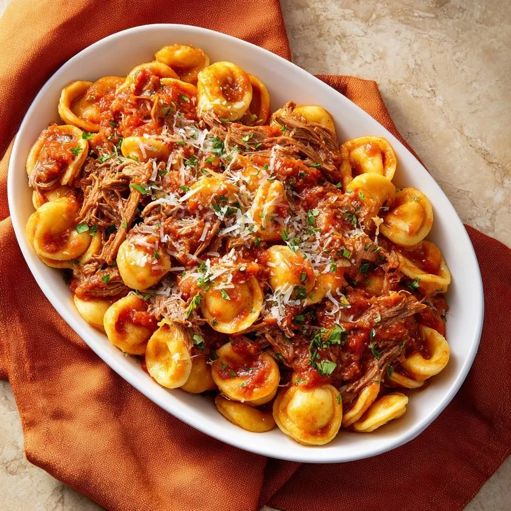 Cheesy tortellini with beef ragu served in a large white oval dish, viewed from directly above.